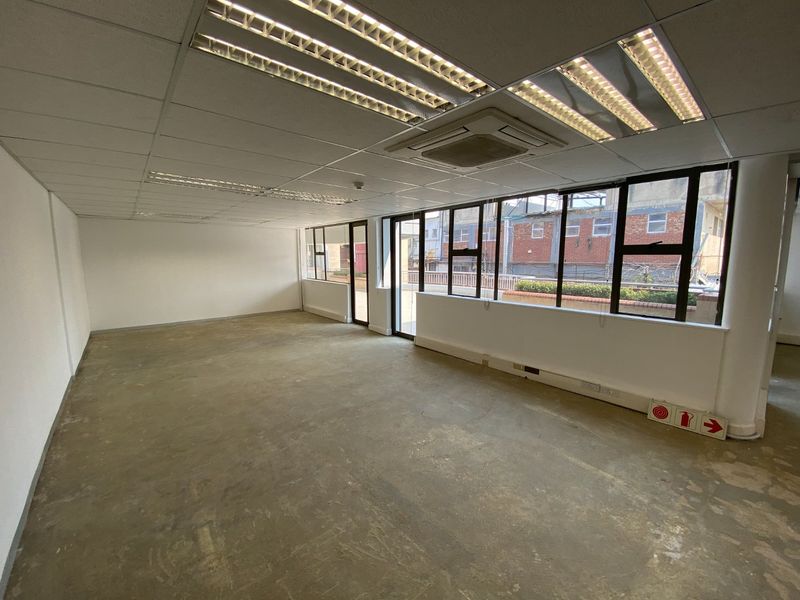 An open-plan commercial office space featuring a suspended ceiling, recessed lighting, integrated air conditioning, and large windows providing natural light.