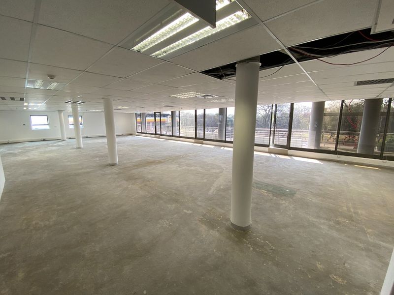 A large, open-plan commercial office space featuring structural columns, expansive windows, and a suspended ceiling requiring maintenance and flooring completion.