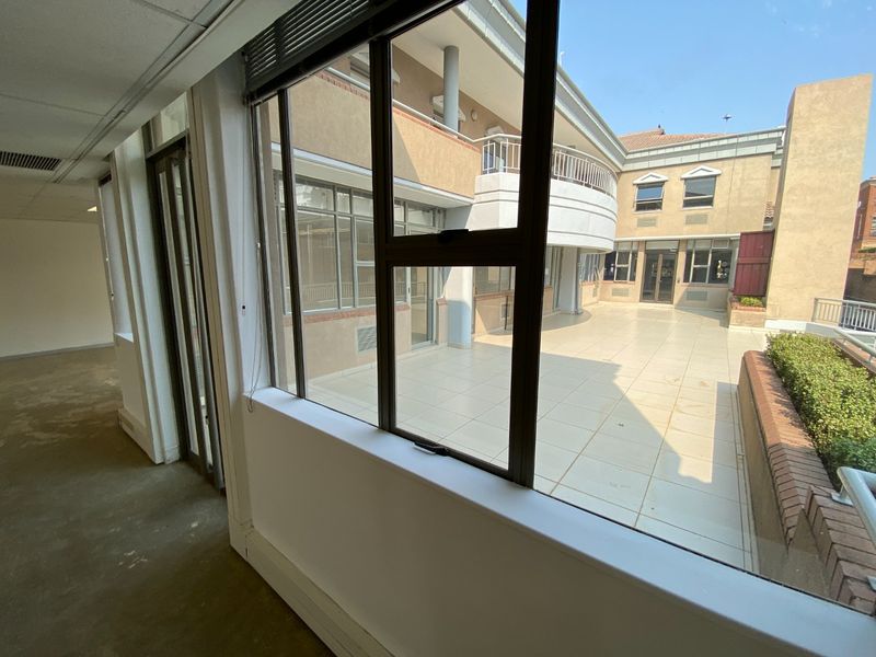A view from an interior office space looking out onto a spacious tiled commercial balcony and courtyard area.