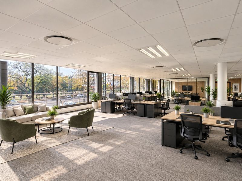 Modern open-plan commercial office space featuring large floor-to-ceiling windows, suspended ceilings, recessed lighting, and high-quality carpeted flooring with glass-partitioned meeting areas.
