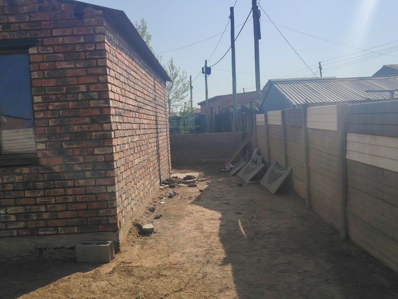 A side view of the property showing a face brick exterior wall and a precast concrete boundary fence with an unpaved yard area.