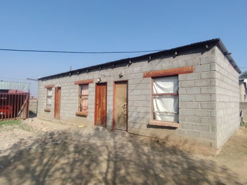 A single-story residential structure featuring exposed concrete block walls, a corrugated metal roof, and multiple entry points.