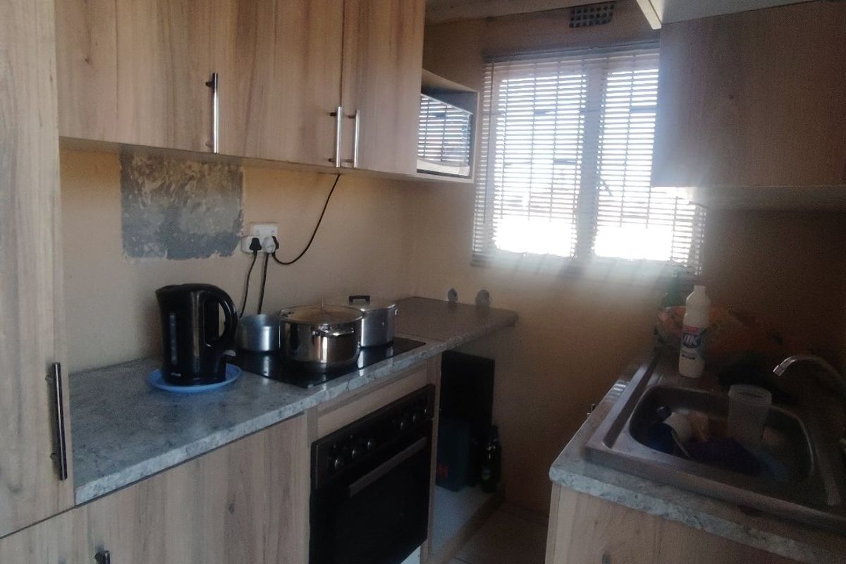 Compact kitchen featuring wood-look cabinetry, laminate countertops, built-in oven, electric hob, and a stainless steel sink with tiled flooring.
