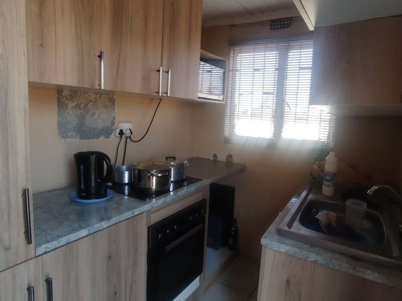 Compact kitchen featuring wood-look cabinetry, laminate countertops, built-in oven, electric hob, and a stainless steel sink with tiled flooring.