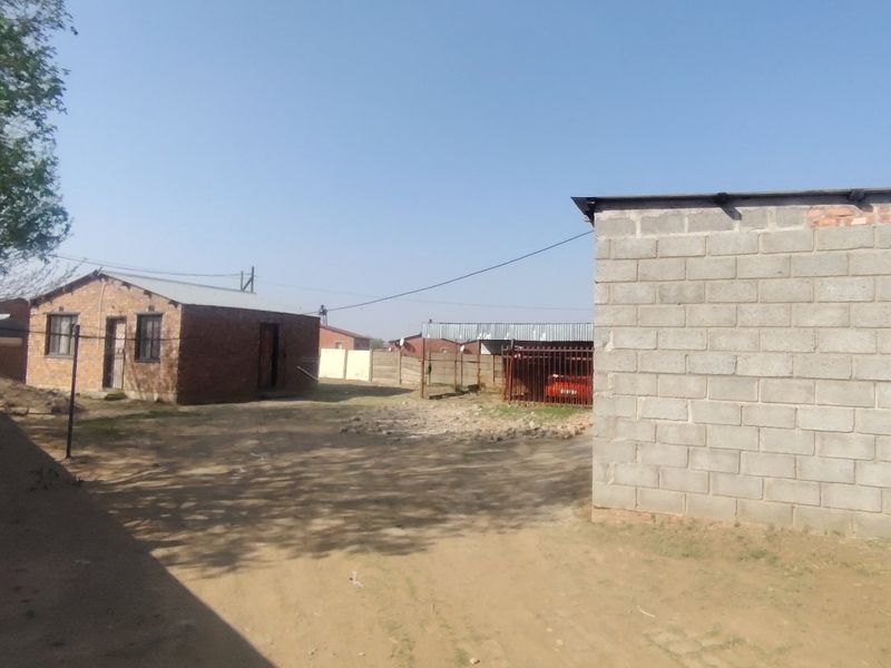 A view of the rear yard area featuring an exposed brick structure and a concrete block wall with unpaved ground.