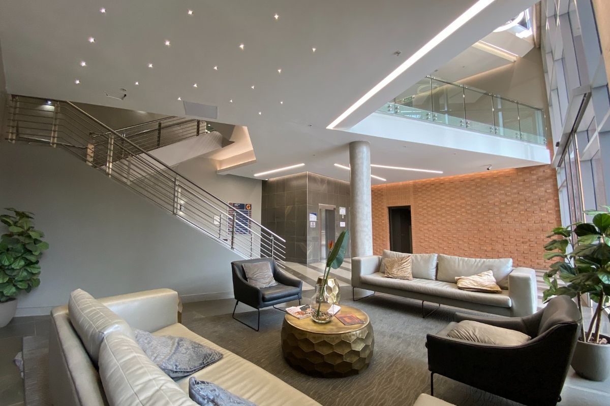 Modern commercial building lobby featuring a grand staircase, glass mezzanine, exposed brick accent wall, and high-end recessed and linear lighting design.