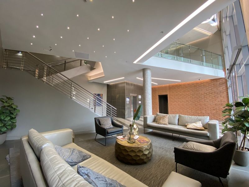 Modern commercial building lobby featuring a grand staircase, glass mezzanine, exposed brick accent wall, and high-end recessed and linear lighting design.