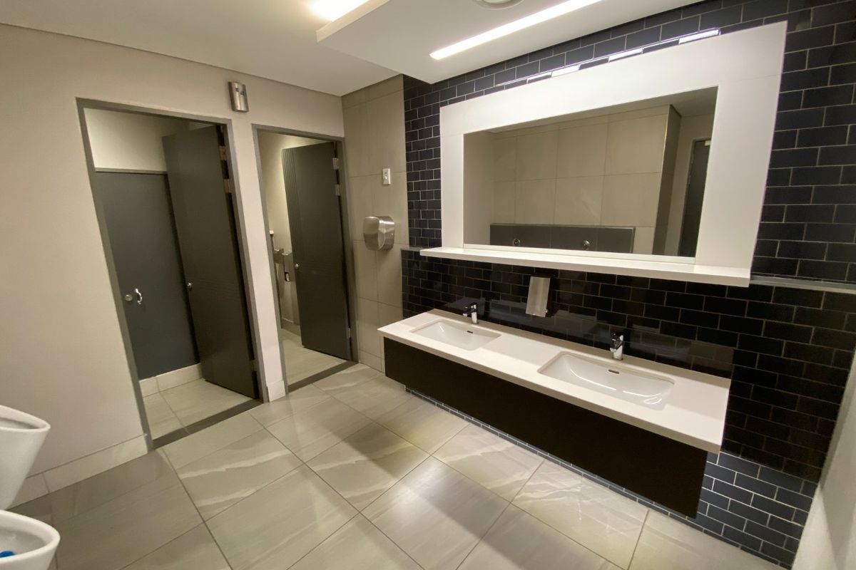 Modern commercial bathroom featuring a sleek double vanity with integrated sinks, large wall-mounted mirror, and contemporary dark subway tile accents.