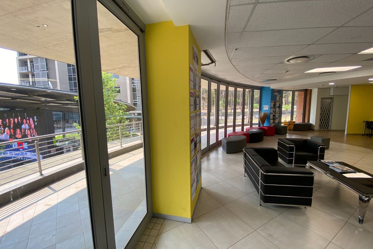 Spacious commercial lounge area featuring large glass sliding doors leading to a balcony, tiled flooring, and a modern suspended ceiling with recessed lighting.