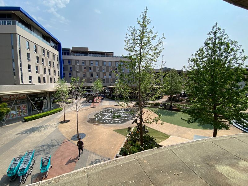 An elevated view of a commercial courtyard featuring a central water fountain, landscaped garden areas, and surrounding multi-story retail and office building facades.