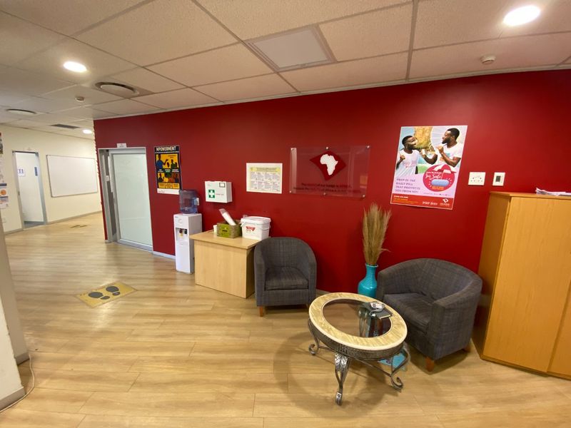 A commercial reception or waiting area featuring laminate flooring, a suspended ceiling with recessed lighting, and a prominent red accent wall.