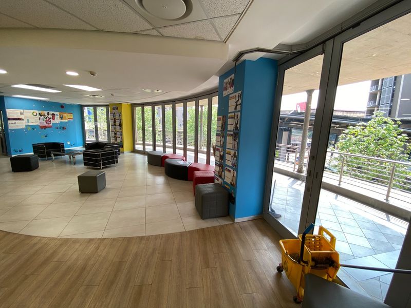Spacious open-plan commercial area featuring a mix of tiled and wood-look flooring, recessed lighting, and large glass doors leading to an outdoor balcony.