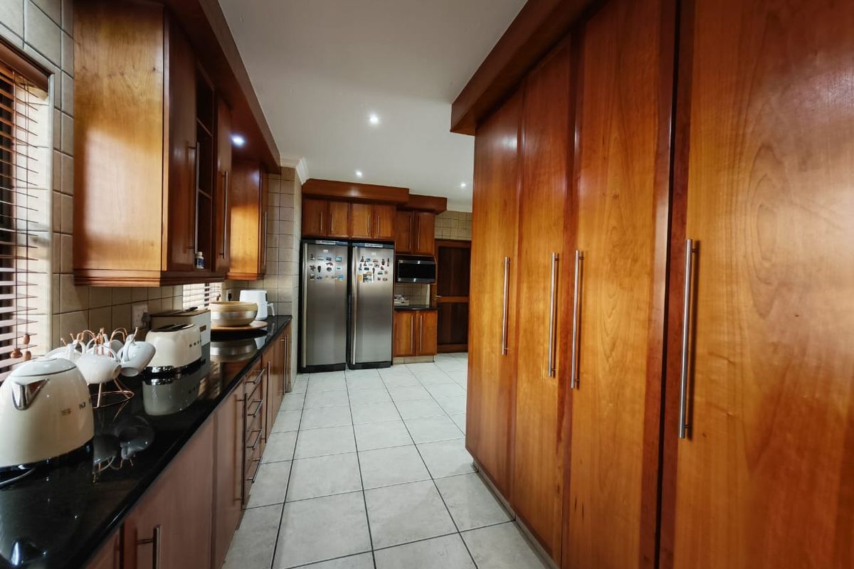A spacious kitchen featuring extensive built-in wooden cabinetry, granite countertops, and tiled flooring, offering ample storage and a functional layout.
