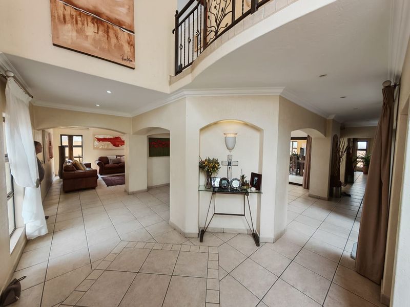 Spacious double-volume entrance hall featuring tiled flooring, decorative archways, a built-in wall niche, and an elegant wrought iron staircase balustrade.