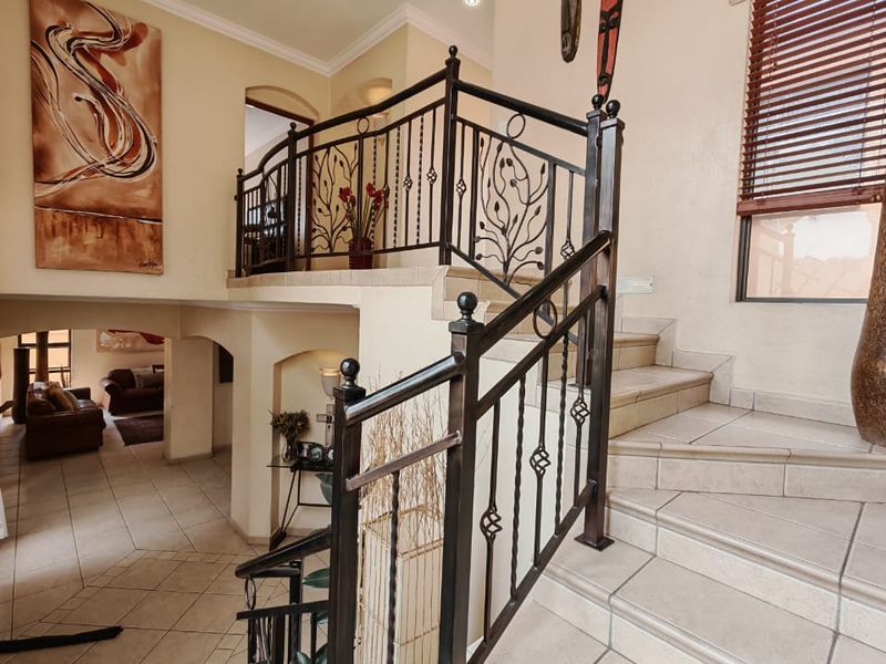 Spacious entrance hall featuring a tiled staircase with decorative wrought iron balustrades, recessed lighting, and an open-plan view into the adjacent living area.