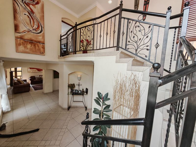 Spacious entrance hall featuring a grand staircase with decorative wrought iron railings, tiled flooring, and a built-in wall niche.