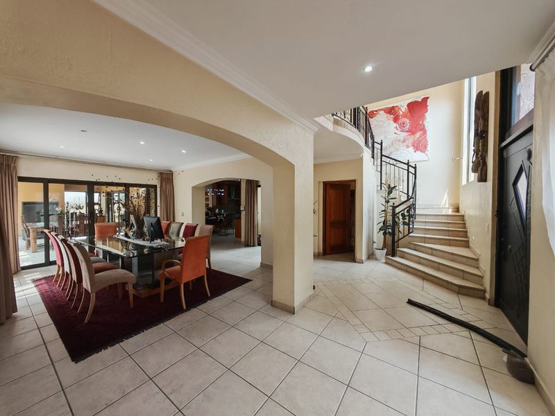 Spacious open-plan living and dining area featuring tiled floors, arched transitions, and a grand staircase with wrought iron detailing.
