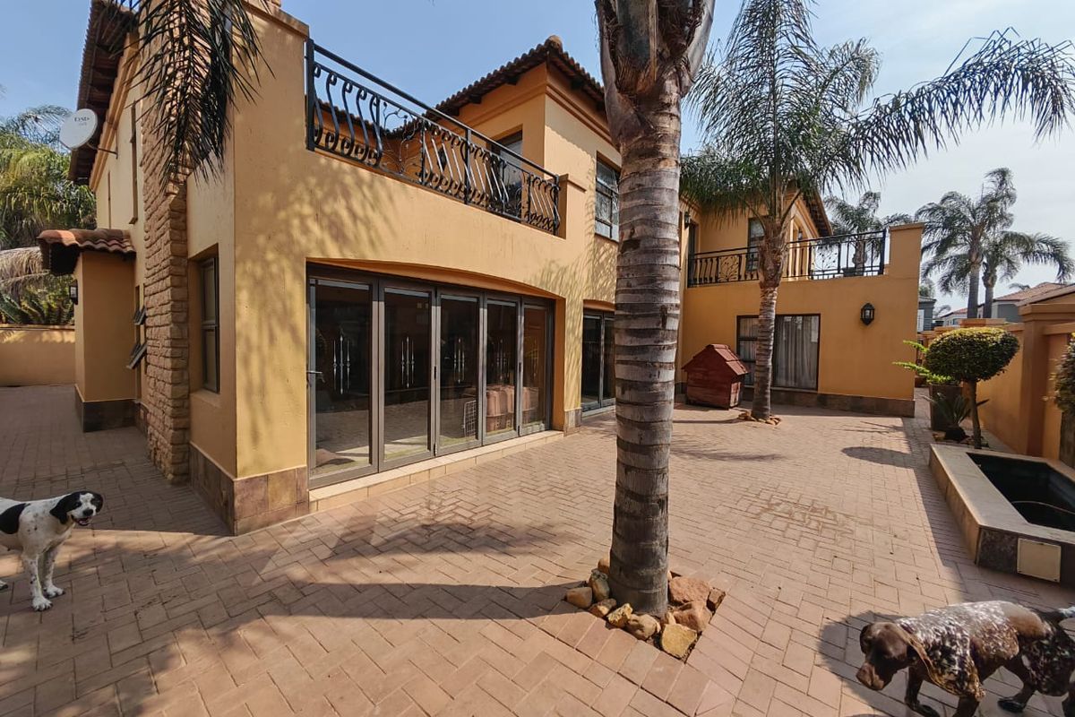 Spacious rear patio area featuring paved flooring, stacking glass doors leading to the interior, and an upper-level balcony with wrought iron railings.
