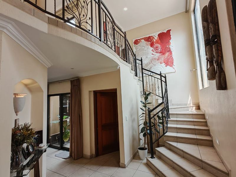 Spacious double-volume entrance hall featuring a grand tiled staircase with decorative wrought iron balustrades and modern recessed lighting.