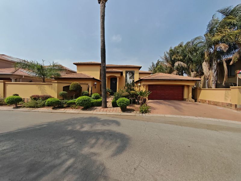 Front elevation of a Mediterranean-style house featuring a tiled roof, integrated double garage, and established landscaped garden with a paved driveway.