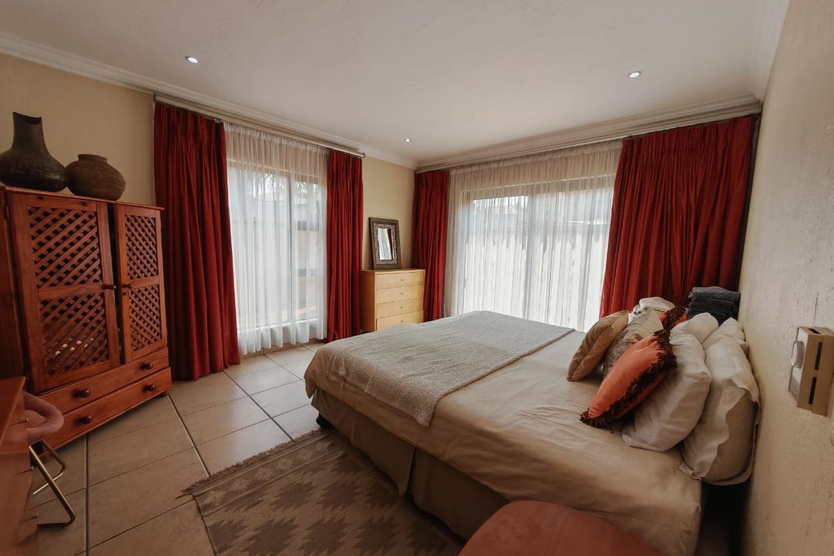 Spacious bedroom featuring tiled flooring, recessed lighting, and large sliding glass doors with floor-to-ceiling curtains providing access to the exterior.