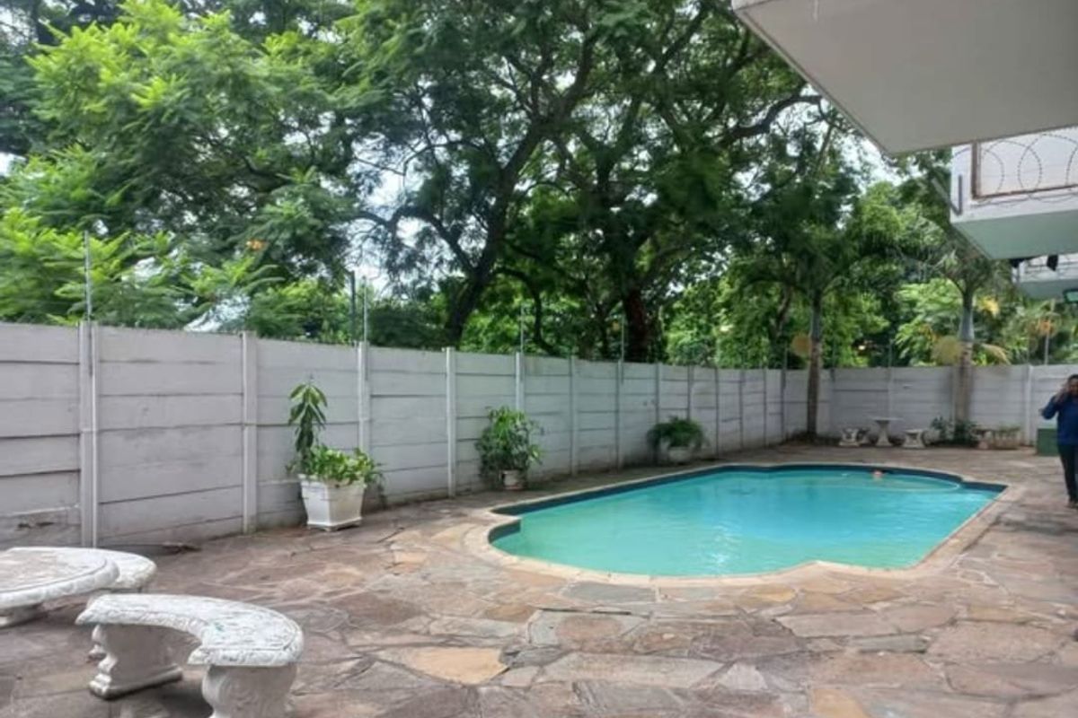 Outdoor pool area featuring stone paving, a swimming pool, and a perimeter precast concrete wall with security fencing.