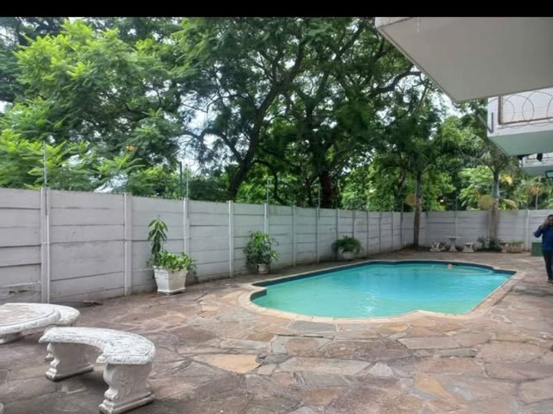 Outdoor pool area featuring stone paving, a swimming pool, and a perimeter precast concrete wall with security fencing.
