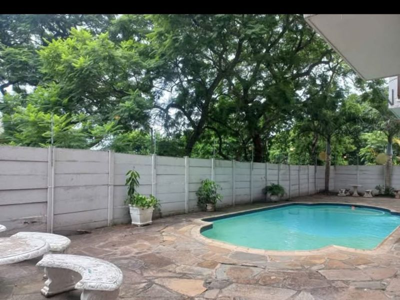 Outdoor pool area featuring stone paving, a swimming pool, and a secure precast concrete boundary wall with electric fencing.