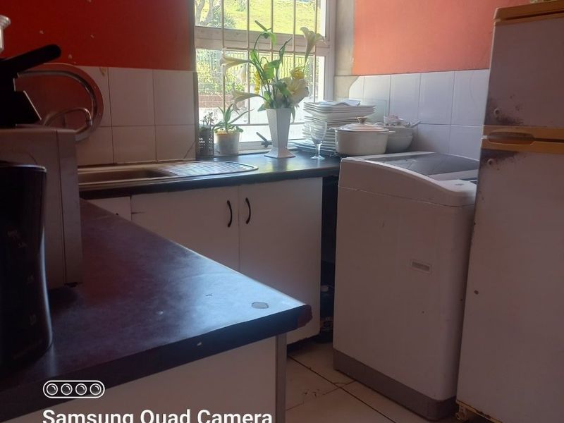 A compact kitchen featuring laminate countertops, a stainless steel sink, and tiled splashbacks, requiring cosmetic updates to improve its overall aesthetic and functionality.