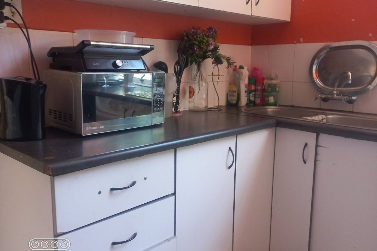 A compact kitchen featuring white cabinetry, laminate countertops, a stainless steel sink, and a tiled backsplash with orange accent walls.