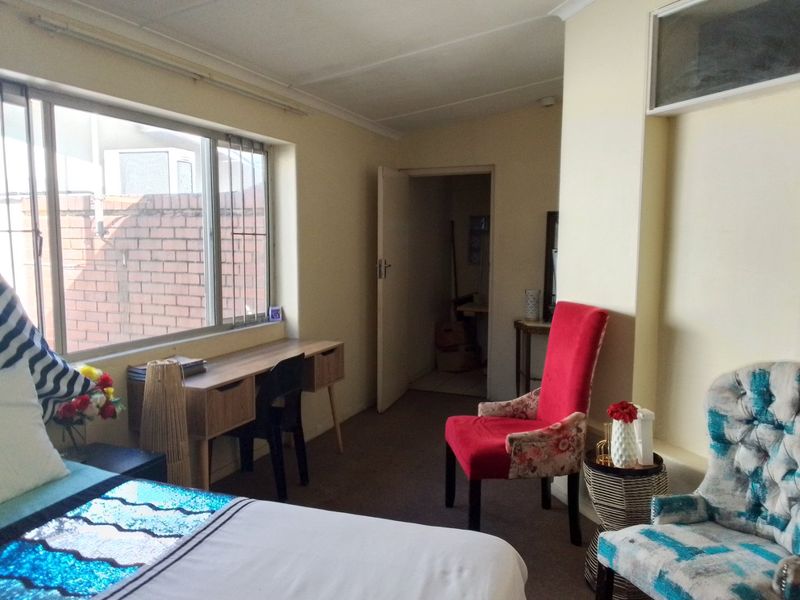 A bedroom featuring carpeted flooring and a large window with aluminium frames, providing natural light and access to an adjacent room.