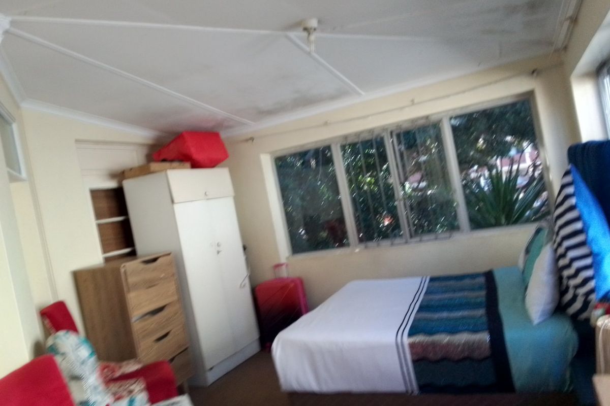 A bedroom featuring a built-in cupboard and large windows with security bars, showing signs of ceiling water damage and wear.