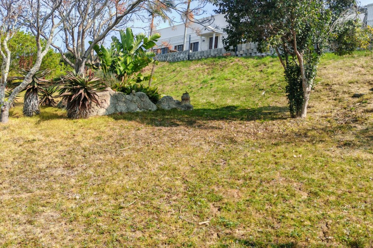 A sloped residential plot featuring established trees, landscaped garden areas, and a concrete block retaining wall at the upper boundary.