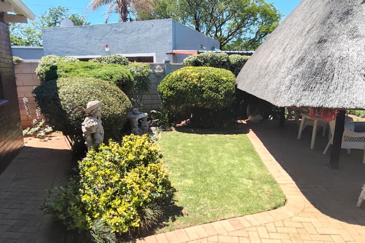 A rear garden area featuring a thatched lapa, brick-paved patio, and established landscaping enclosed by a boundary wall.
