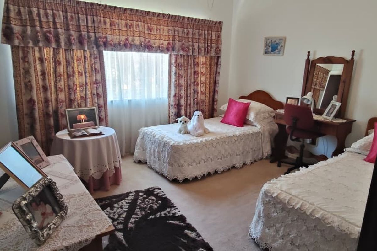 A carpeted bedroom featuring large windows with traditional curtain treatments, offering a functional space with neutral wall finishes.