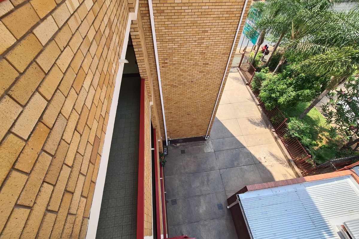 An elevated aerial view of a commercial property featuring a face brick facade, paved courtyard area, and metal perimeter fencing.