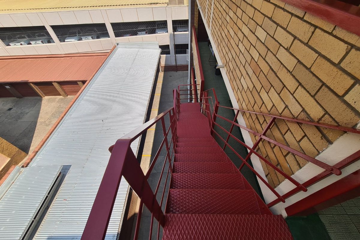 An elevated view of an external metal staircase leading down to a commercial parking area with corrugated roofing.