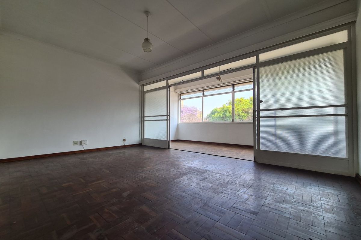 Spacious living area featuring original parquet flooring and large sliding glass doors that open onto an enclosed balcony, providing ample natural light.