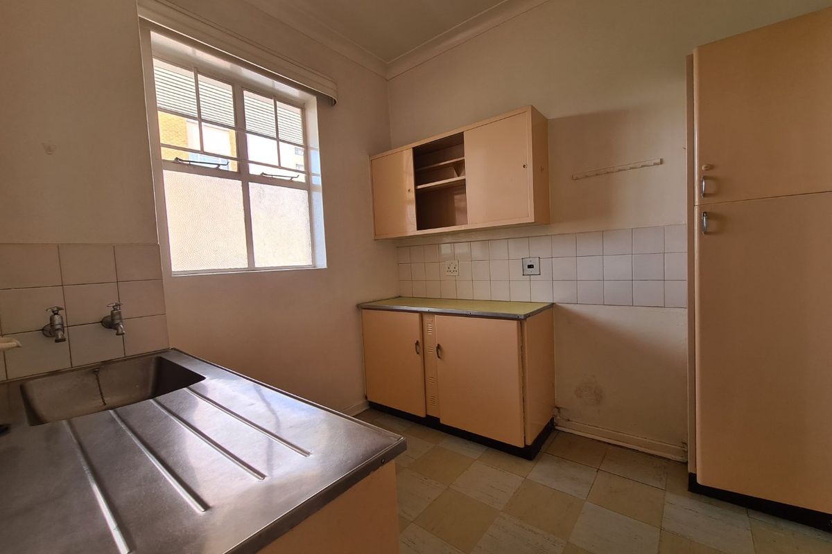 A dated, empty kitchen featuring original cabinetry, a stainless steel sink, and tiled splashbacks, offering a blank canvas for renovation.
