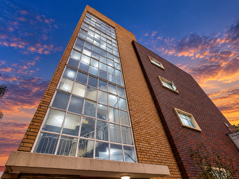 A low-angle view of a multi-story commercial building featuring a prominent glass-enclosed stairwell and a combination of light and dark brick facade finishes.