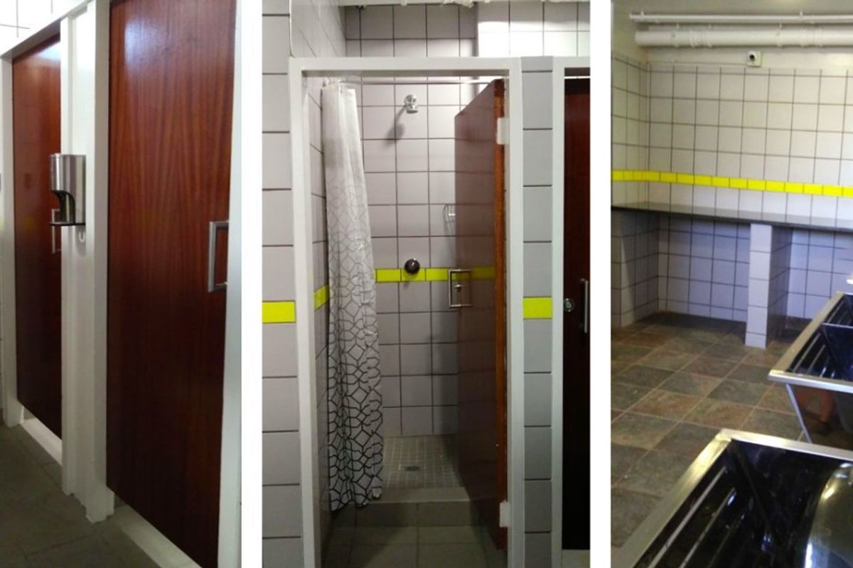 Commercial washroom facility featuring multiple shower stalls, tiled walls, and a row of stainless steel utility sinks.