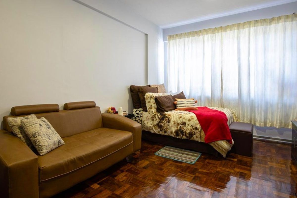 A bedroom featuring polished parquet flooring and large windows with curtains, providing a functional living space.