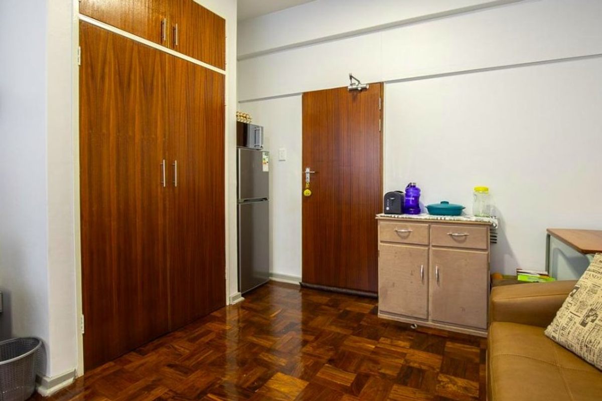 A compact interior space featuring built-in wooden cabinetry, parquet flooring, and a functional layout suitable for a studio or office environment.