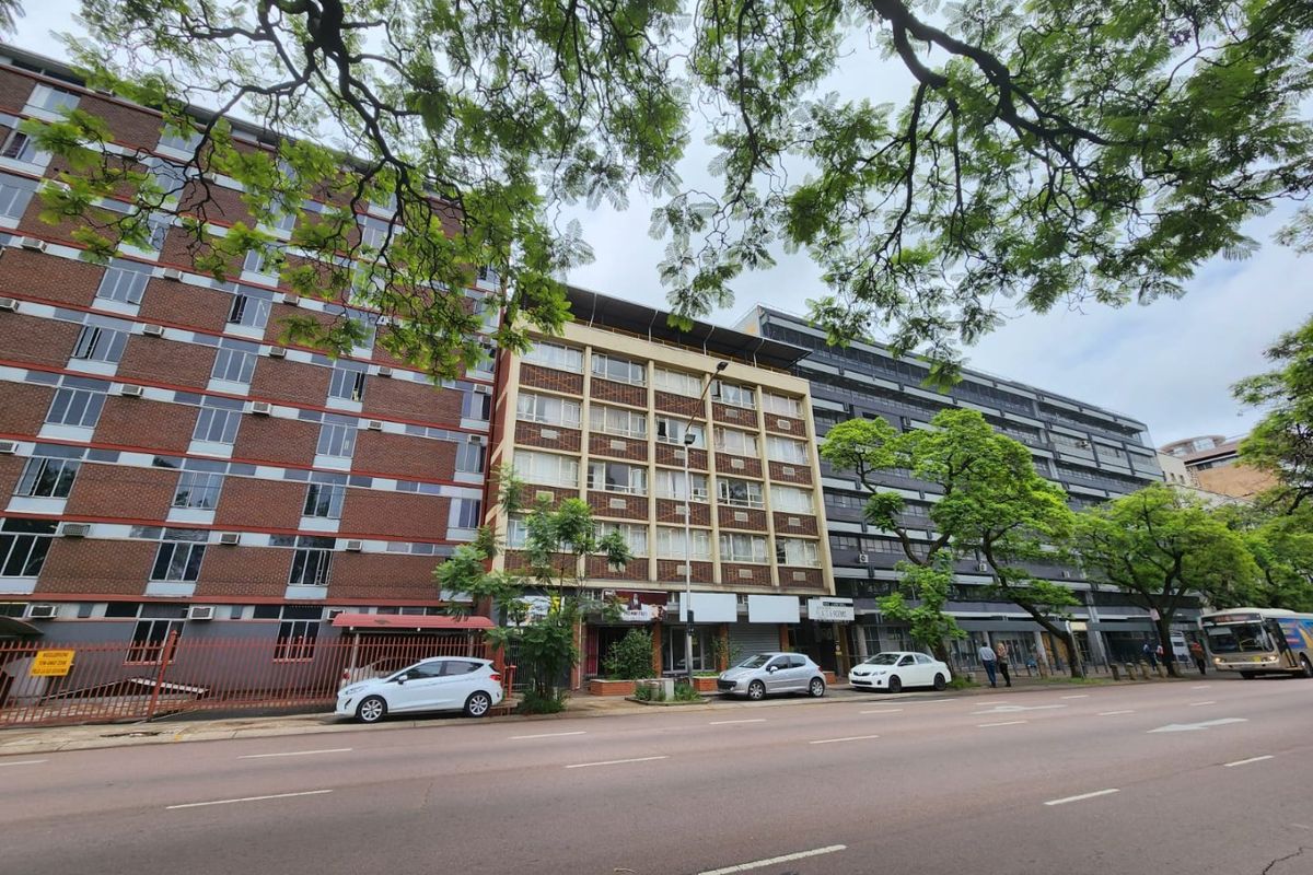 Street view of a multi-story commercial building complex featuring brick and concrete facades with ground-level retail frontage and street-side parking.
