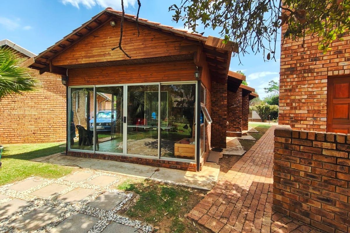 Rear view of the property featuring a brick and timber structure with sliding glass doors and a brick paved pathway leading through the garden.