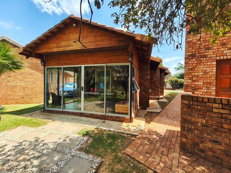 Rear view of the property featuring a brick and timber structure with sliding glass doors and a brick paved pathway leading through the garden.