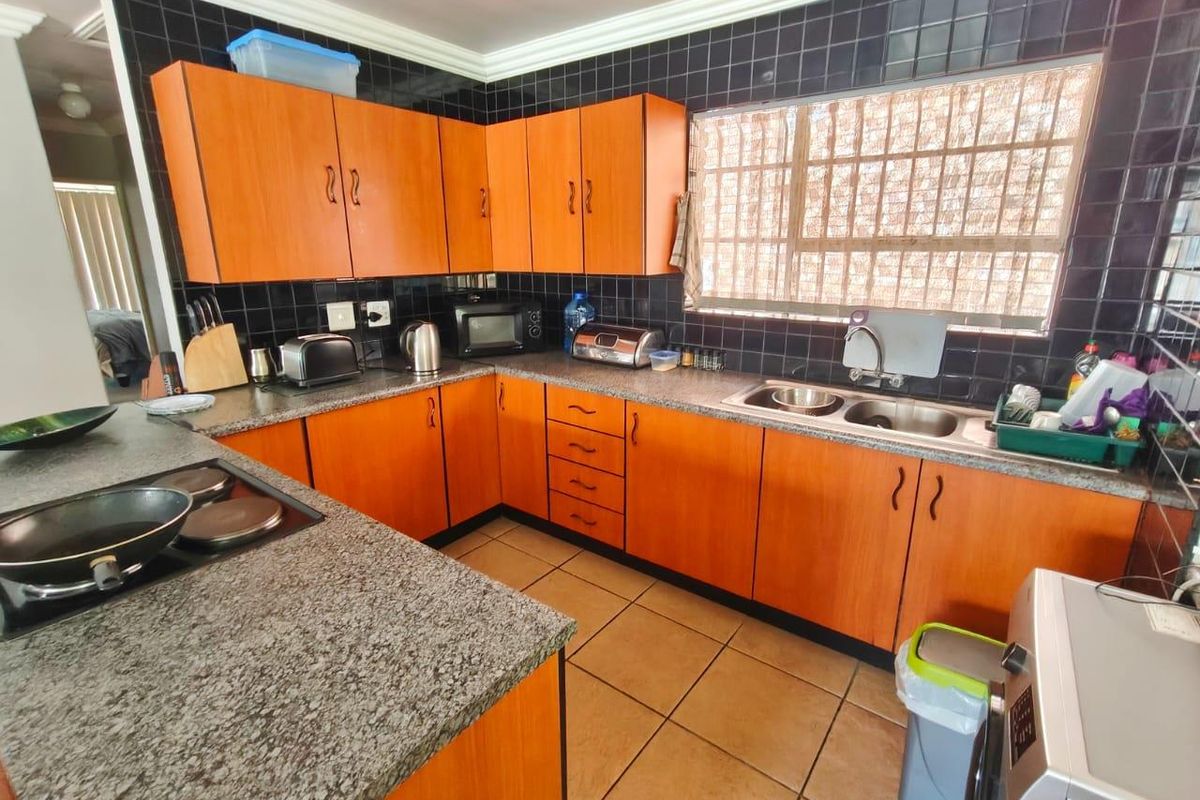 Functional kitchen featuring wood-look cabinetry, granite countertops, a double stainless steel sink, and a tiled backsplash with integrated electric hob.