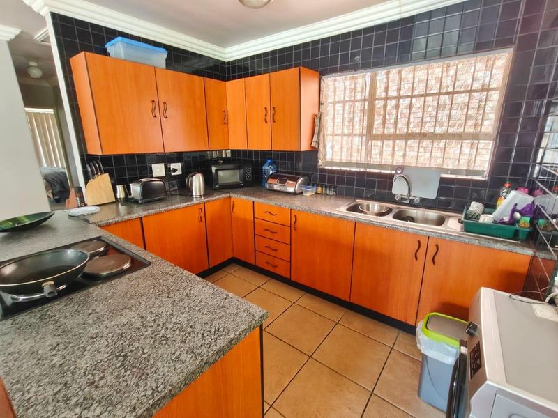 Functional kitchen featuring wood-look cabinetry, granite countertops, a double stainless steel sink, and a tiled backsplash with integrated electric hob.