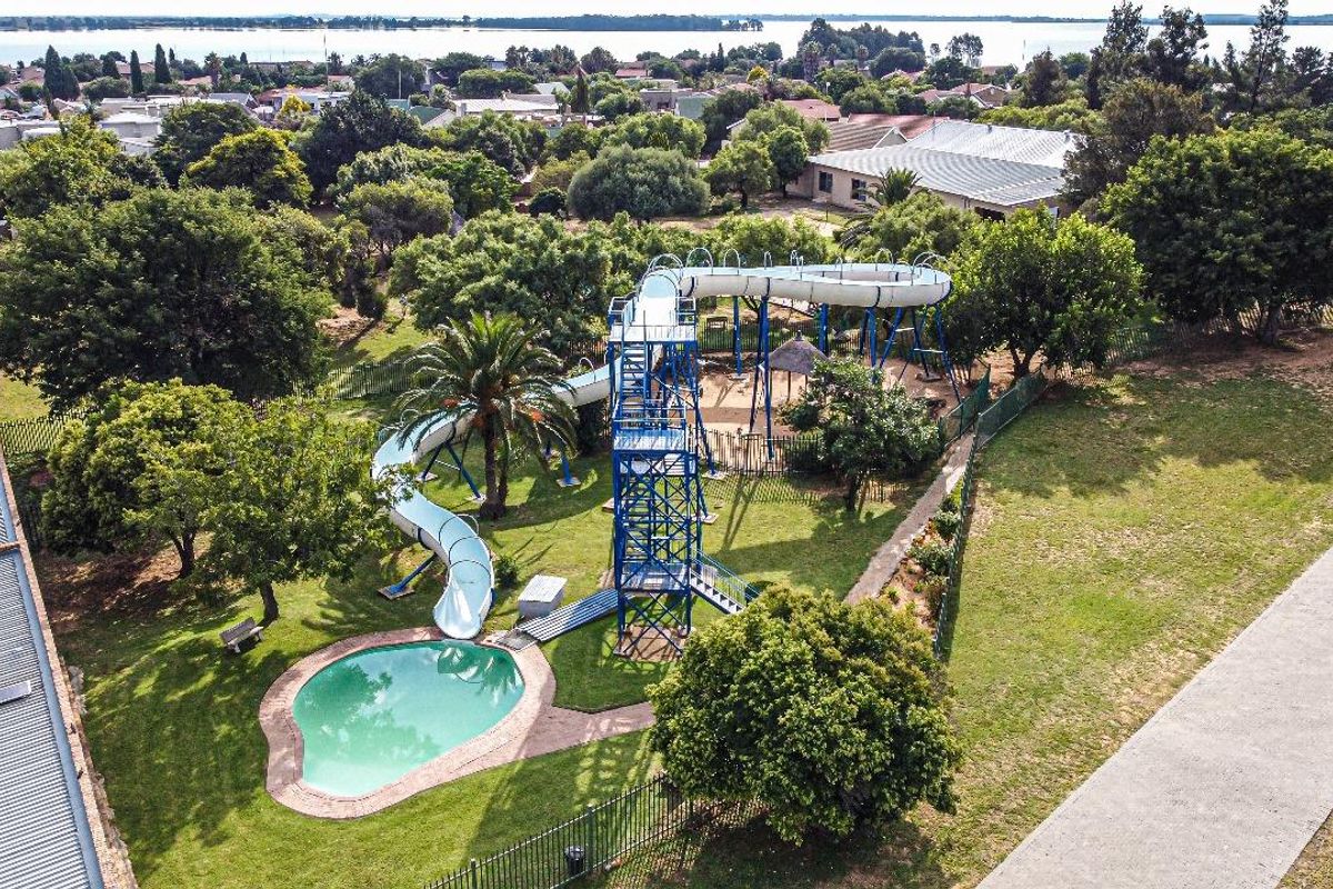 Aerial view of a recreational area featuring a swimming pool, a large water slide structure, and surrounding landscaped garden space.