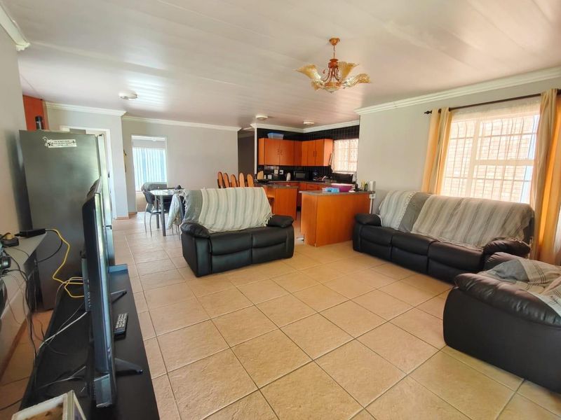 Spacious open-plan living and kitchen area featuring tiled flooring, functional cabinetry, and natural light through windows with security bars.